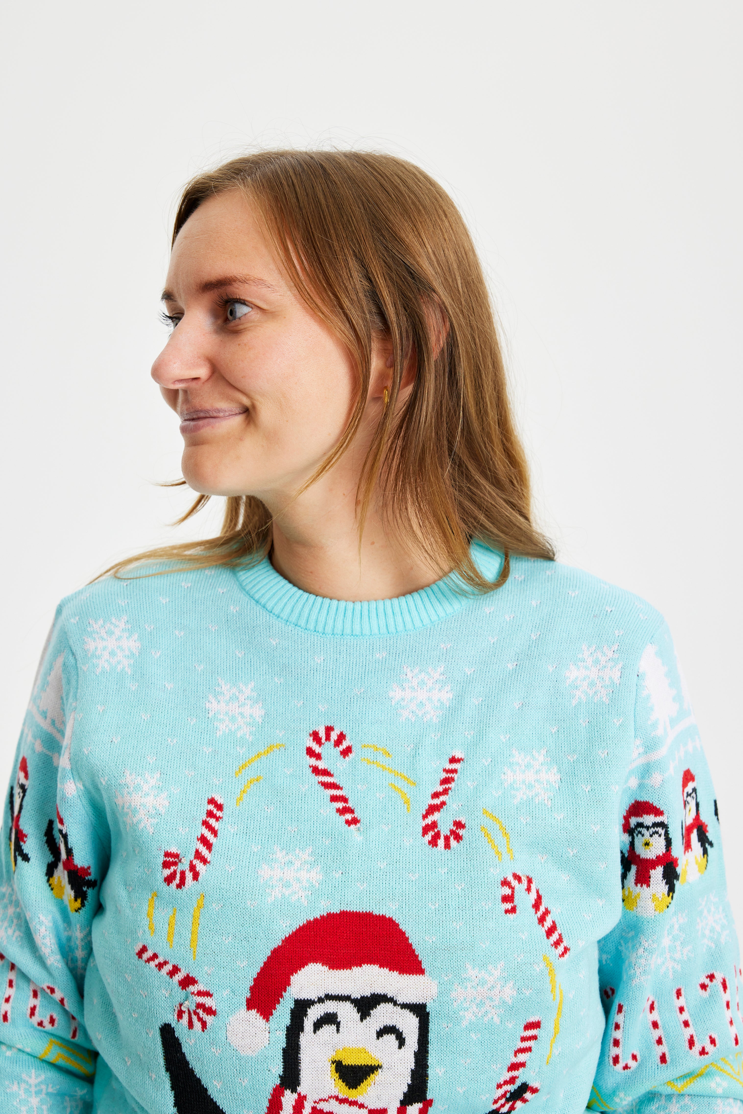 En dame kigger til siden og er iført en julesweater med pingviner og sukkerstokke på.